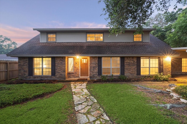 traditional home with a shingled roof, brick siding, and a lawn