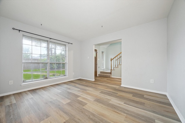 spare room with stairway, light wood-style flooring, and baseboards