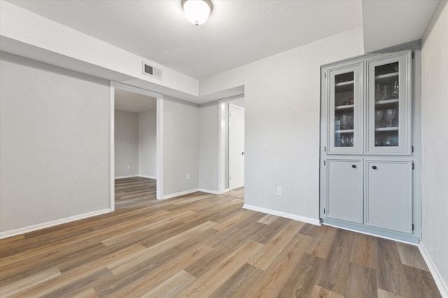 unfurnished room featuring a textured ceiling, wood finished floors, visible vents, and baseboards