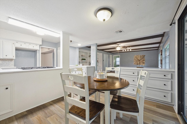 dining room with light wood-type flooring, a textured ceiling, visible vents, and beamed ceiling