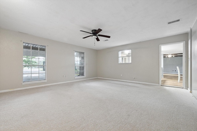 empty room featuring ceiling fan, visible vents, baseboards, and light colored carpet