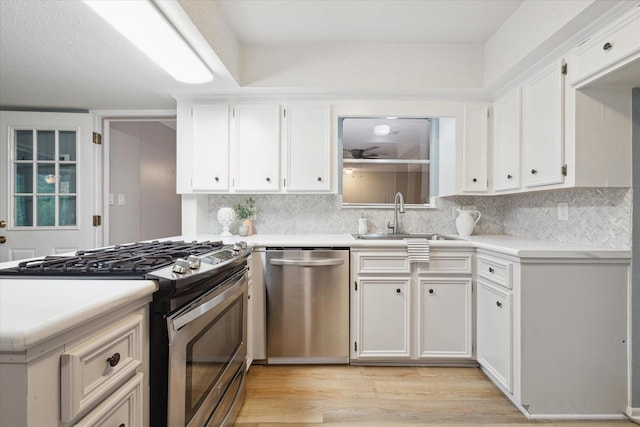 kitchen with stainless steel appliances, light countertops, white cabinetry, a sink, and light wood-type flooring