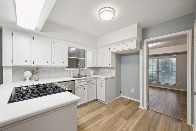 kitchen featuring white cabinets, backsplash, light countertops, and a sink