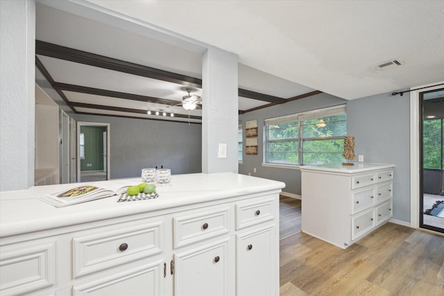 kitchen featuring visible vents, light wood-style floors, white cabinetry, light countertops, and beamed ceiling