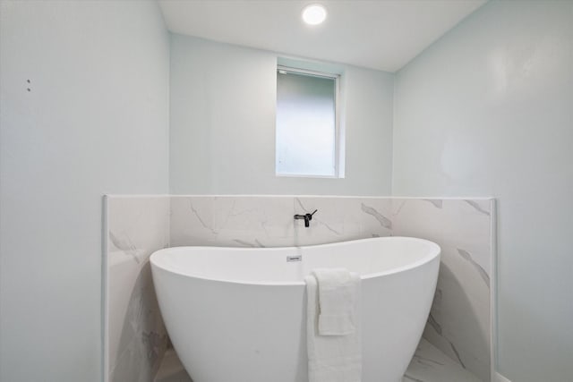 full bath featuring marble finish floor, tile walls, a freestanding bath, and a wainscoted wall