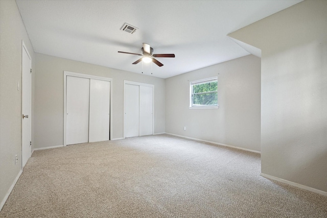 unfurnished bedroom featuring visible vents, baseboards, ceiling fan, carpet flooring, and multiple closets