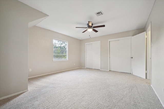 unfurnished bedroom featuring two closets, light colored carpet, visible vents, a ceiling fan, and baseboards