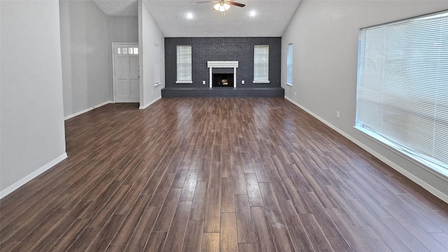 unfurnished living room with dark hardwood / wood-style flooring, a brick fireplace, a textured ceiling, ceiling fan, and high vaulted ceiling