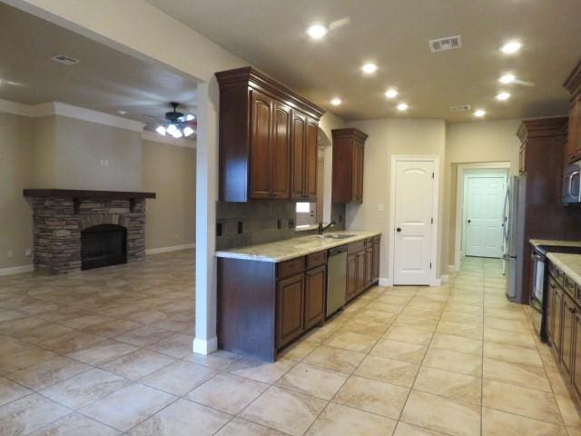 kitchen with appliances with stainless steel finishes, backsplash, dark brown cabinetry, ceiling fan, and a stone fireplace