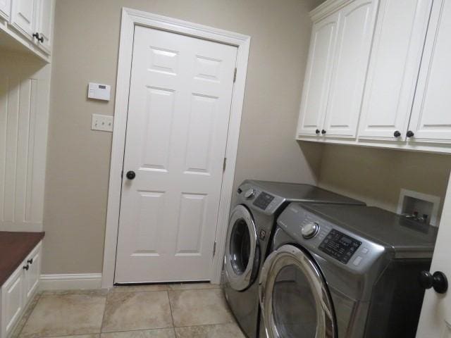 laundry room featuring washing machine and clothes dryer, light tile patterned floors, and cabinets