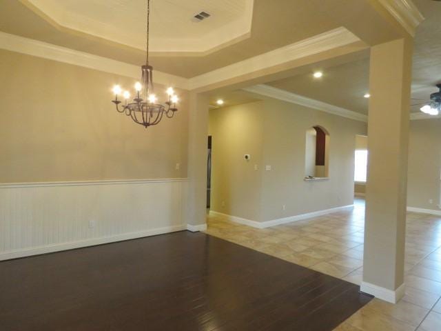 tiled empty room featuring a tray ceiling, ceiling fan with notable chandelier, and ornamental molding