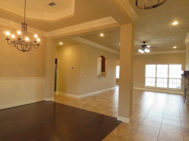 tiled empty room with ceiling fan with notable chandelier, a tray ceiling, and ornamental molding