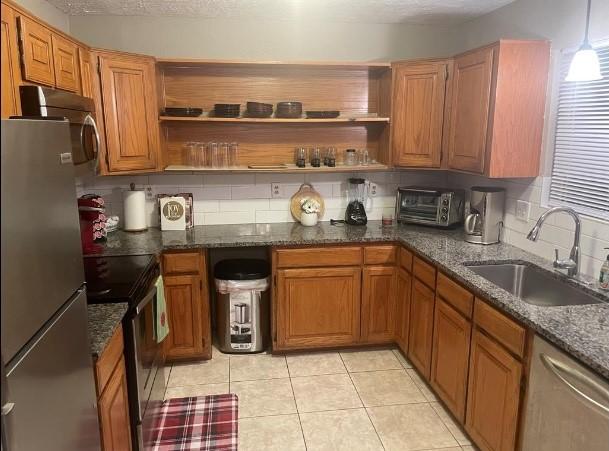 kitchen featuring stainless steel appliances, sink, light tile patterned floors, dark stone countertops, and hanging light fixtures