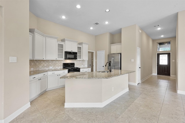 kitchen with light stone countertops, a kitchen island with sink, sink, black appliances, and white cabinets