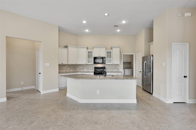 kitchen with light stone counters, a kitchen island with sink, black appliances, white cabinets, and washer / clothes dryer