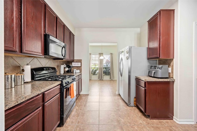 kitchen featuring decorative backsplash, appliances with stainless steel finishes, light stone countertops, hanging light fixtures, and light tile patterned flooring