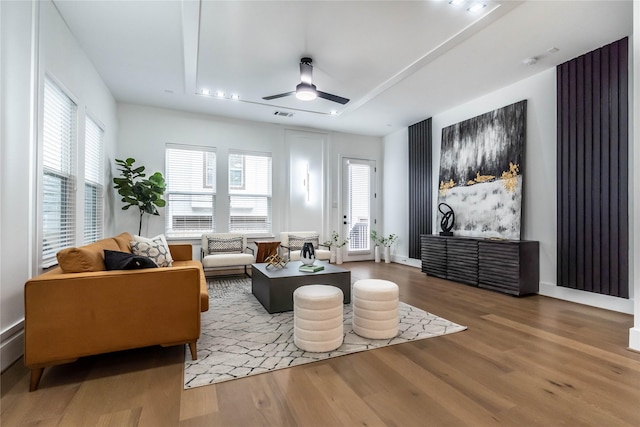 living area featuring a raised ceiling, ceiling fan, and hardwood / wood-style flooring