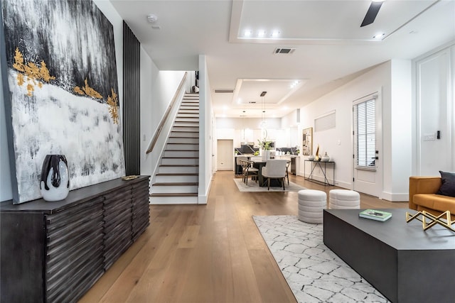 living room featuring light hardwood / wood-style floors, a raised ceiling, and ceiling fan