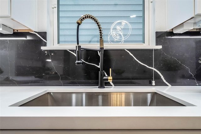 interior details with sink, white cabinetry, and backsplash