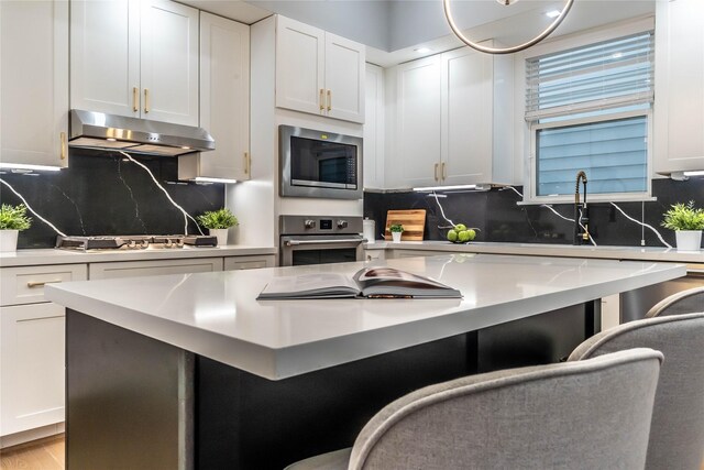 kitchen with a kitchen breakfast bar, light hardwood / wood-style flooring, decorative backsplash, white cabinets, and appliances with stainless steel finishes