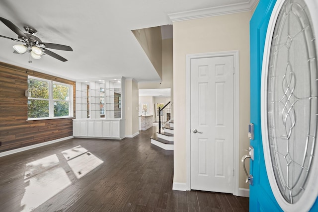 foyer with ceiling fan, wood walls, ornamental molding, and dark wood-type flooring