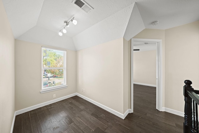 empty room with a textured ceiling, dark hardwood / wood-style flooring, track lighting, and lofted ceiling