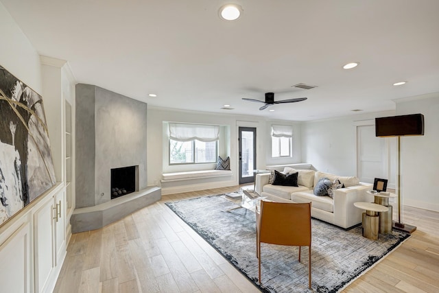 living room with a fireplace, light hardwood / wood-style floors, ceiling fan, and crown molding