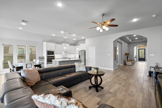 living room featuring sink, light wood-type flooring, a wealth of natural light, and ceiling fan