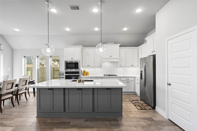 kitchen with a center island with sink, white cabinets, pendant lighting, and appliances with stainless steel finishes