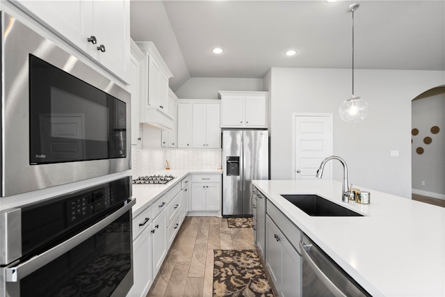 kitchen with appliances with stainless steel finishes, sink, white cabinets, light hardwood / wood-style floors, and hanging light fixtures