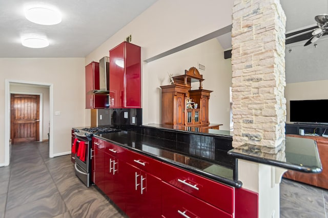 kitchen featuring gas stove, ceiling fan, wall chimney range hood, decorative columns, and vaulted ceiling