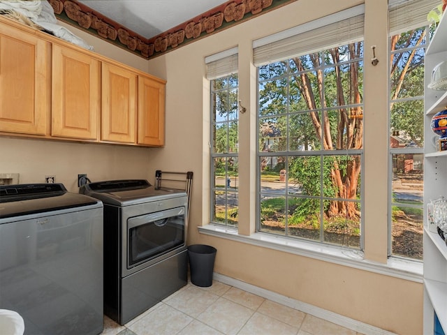 clothes washing area with cabinets, plenty of natural light, washer and dryer, and light tile patterned flooring