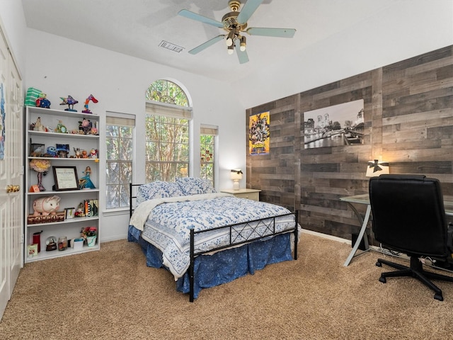 carpeted bedroom featuring ceiling fan and wooden walls