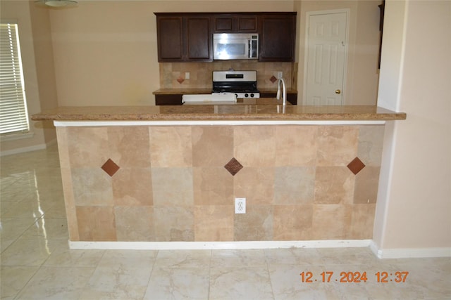 kitchen with backsplash, white range with gas stovetop, sink, kitchen peninsula, and dark brown cabinetry