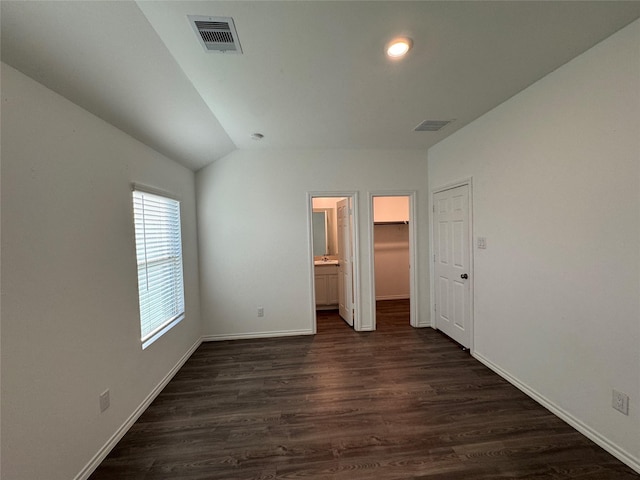 unfurnished bedroom featuring ensuite bath, a spacious closet, dark wood-type flooring, and vaulted ceiling