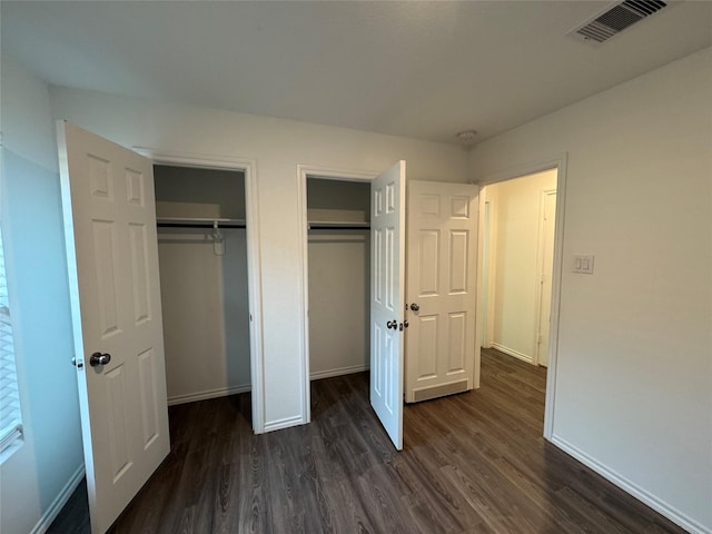 unfurnished bedroom featuring two closets and dark hardwood / wood-style floors