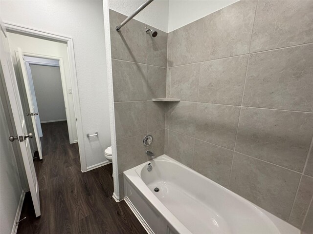 bathroom with hardwood / wood-style floors, tiled shower / bath combo, and toilet