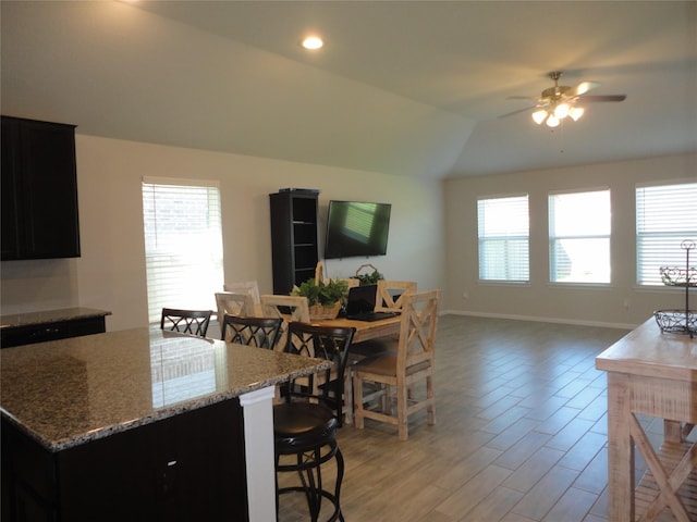 kitchen featuring vaulted ceiling, ceiling fan, light stone countertops, light wood-type flooring, and a breakfast bar area