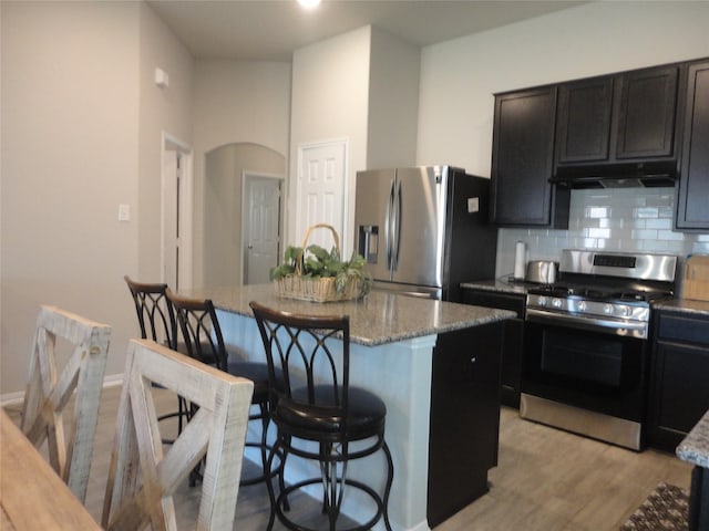 kitchen featuring light stone countertops, backsplash, stainless steel appliances, a center island, and light hardwood / wood-style floors