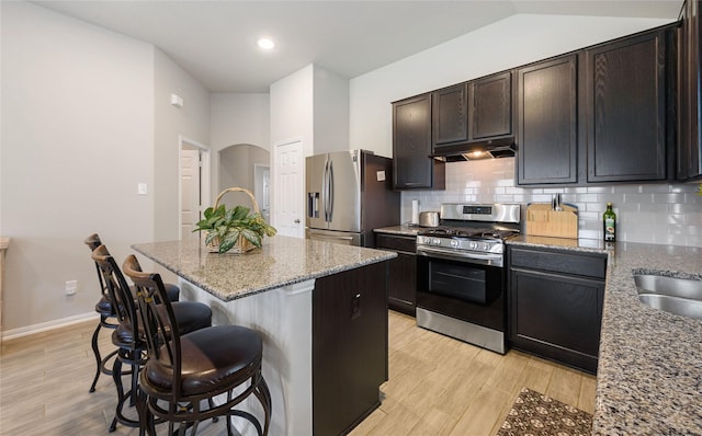 kitchen featuring a kitchen breakfast bar, light stone counters, light hardwood / wood-style flooring, and stainless steel appliances