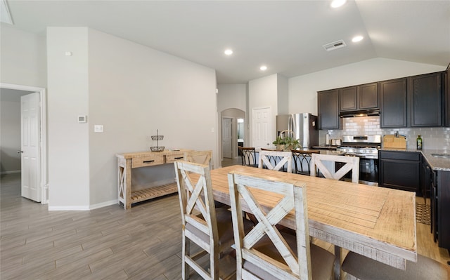 kitchen with dark brown cabinetry, backsplash, lofted ceiling, appliances with stainless steel finishes, and light wood-type flooring