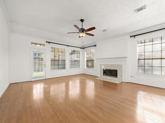 unfurnished living room with ceiling fan, a textured ceiling, a high end fireplace, and light hardwood / wood-style floors