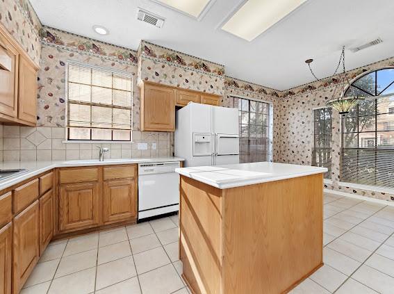 kitchen with white appliances, light tile patterned flooring, decorative backsplash, and a kitchen island