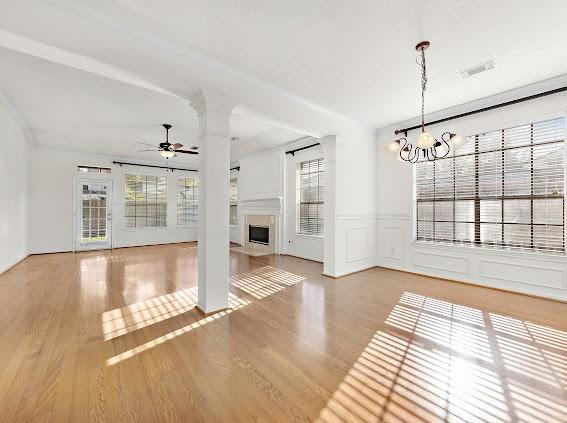 unfurnished living room with ceiling fan with notable chandelier, light hardwood / wood-style flooring, and ornate columns