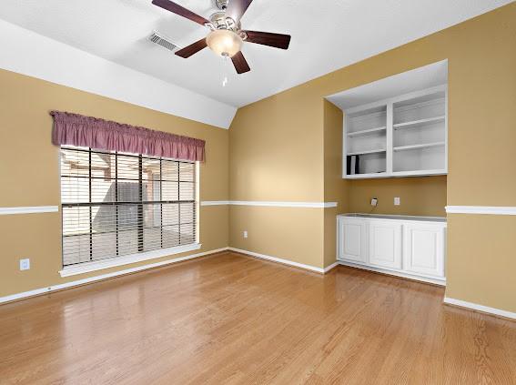 spare room with vaulted ceiling, ceiling fan, light hardwood / wood-style floors, and built in shelves