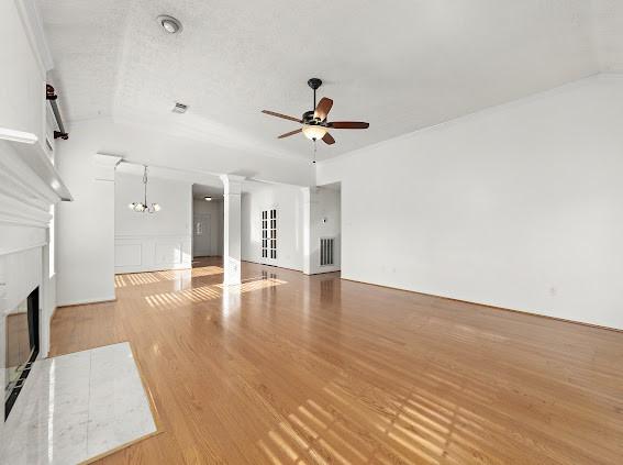 unfurnished living room with vaulted ceiling, decorative columns, ceiling fan with notable chandelier, and light hardwood / wood-style flooring