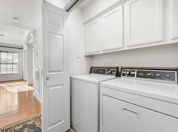 laundry room with independent washer and dryer, light hardwood / wood-style floors, and cabinets