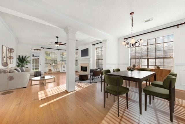 dining area with decorative columns, crown molding, ceiling fan with notable chandelier, and light hardwood / wood-style flooring