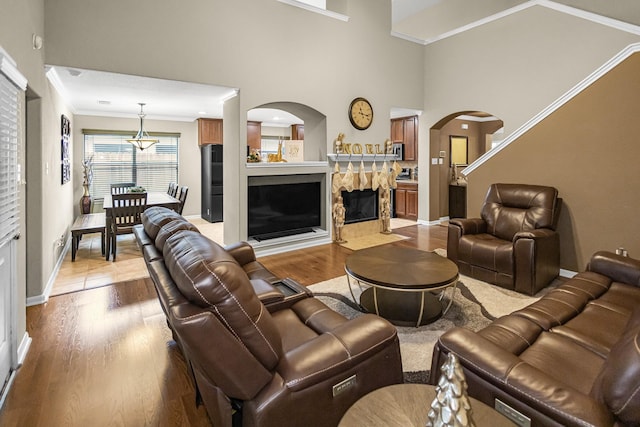 living room featuring crown molding, a fireplace, a high ceiling, and light wood-type flooring