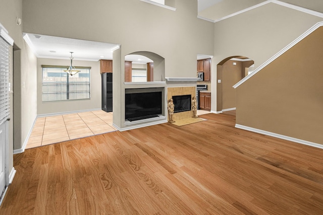 unfurnished living room featuring crown molding, a tile fireplace, light hardwood / wood-style flooring, and a high ceiling